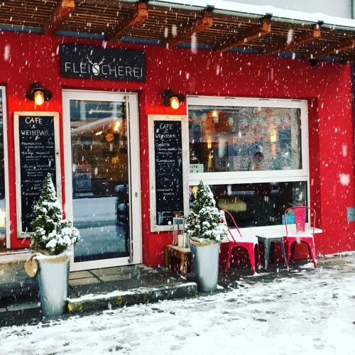a red building with a table and chairs in the snow at Fleischerei - Apartments, Cafe & Weinbar in Hinterstoder