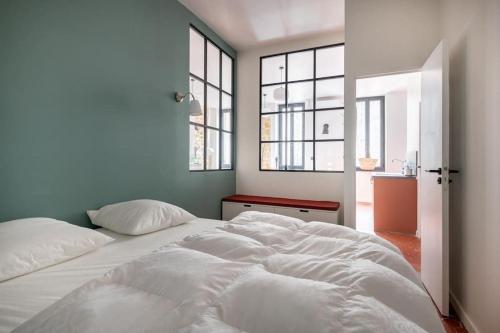 un grand lit blanc dans une pièce avec des fenêtres dans l'établissement T2 typique et décoré avec goût - quartier Vauban, à Marseille