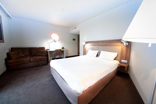 a bedroom with a large white bed and a couch at Campanile Clermont Ferrand Centre in Clermont-Ferrand
