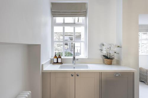 a white kitchen with a sink and a window at Wharton Cottage, Lake District Retreat in Cartmel