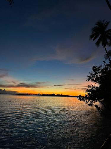 a sunset over a body of water with a palm tree at Fam Homestay in Fam