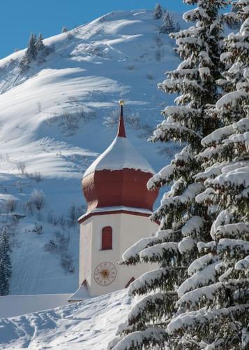 a building with a clock tower in the snow at Sonniges Bergblick-Appartement in Damuls