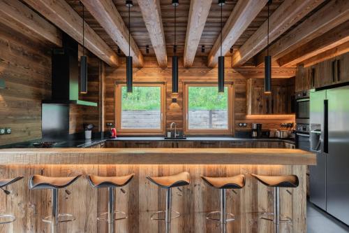une cuisine avec des placards en bois et un bar avec des tabourets dans l'établissement Chalet Luxe piscine et spa 18 personnes serrechevalierholidays, au Monêtier-les-Bains
