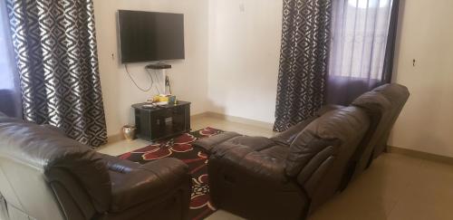 a living room with a leather couch and a television at 12 minutes by walk from ocean in Brufut