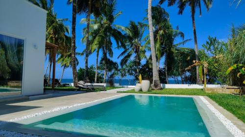 a swimming pool in front of a house with palm trees at Villa Shepherd Zanzibar - LUXURY BEACH FRONT - KIWENGWA in Kumba Urembo