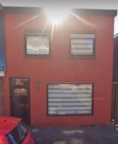 a red building with two windows and a car parked in front at Smile Home Wijk aan Zee 1 in Wijk aan Zee