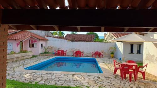 un patio con piscina y mesas y sillas rojas en Jardim Aruan, Caraguatatuba ,sp, en Caraguatatuba