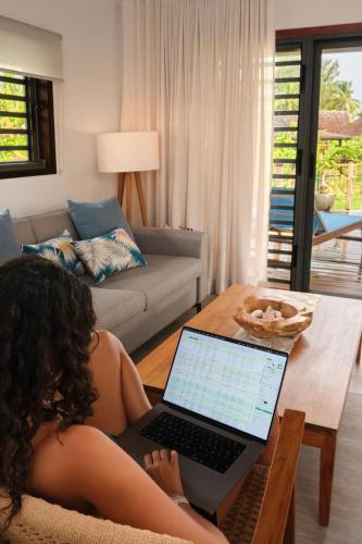 a woman sitting in a chair with a laptop on a table at Moorea Beach Villas in Haapiti