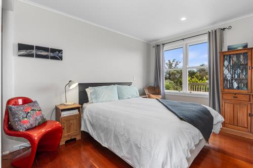 a bedroom with a bed and a red chair and a window at Belmont Beach House - Whangarei Heads Escape in Whangarei