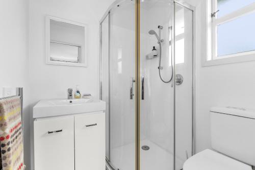 a white bathroom with a shower and a sink at Belmont Beach House - Whangarei Heads Escape in Whangarei