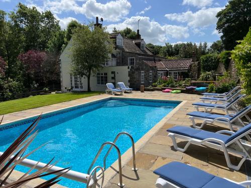 a swimming pool with lounge chairs next to a house at Richmond Hill Cottages, Exclusive 6 bedroom Farm House, Markington with heated pool in Ingerthorpe