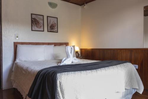 a bedroom with a white bed with two pictures on the wall at Pousada Araucária Suítes in Campos do Jordão