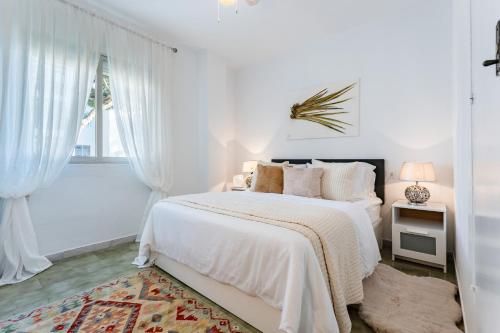 a white bedroom with a bed and a window at Perfekt lokation! Gå til strand, restaurant og by in Sitio de Calahonda