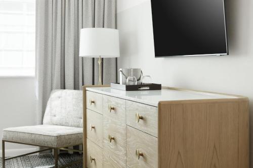 a bedroom with a dresser with a lamp and a chair at Kimpton Surfcomber Hotel by IHG in Miami Beach