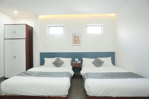 two beds in a room with white walls at Khách sạn Sacly in Kon Tum