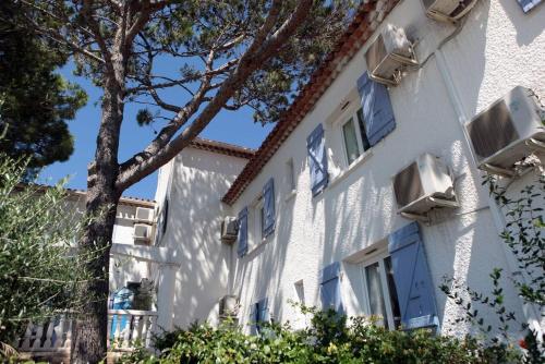 a white building with blue windows and a tree at Le Sarac Hôtel in Clermont-lʼHérault