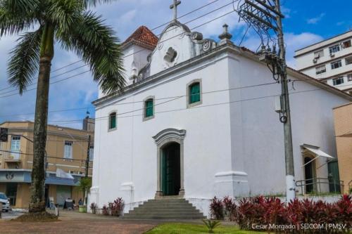 une église blanche avec une tour d'horloge en haut dans l'établissement Apartamento 1013 com varanda e vista ao mar, à São Vicente