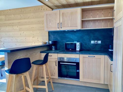 une cuisine avec des placards en bois et deux tabourets bleus dans l'établissement Appartement neuf, lumineux, à 250m des pistes, animaux admis - FR-1-811-4, à Les Deux Alpes