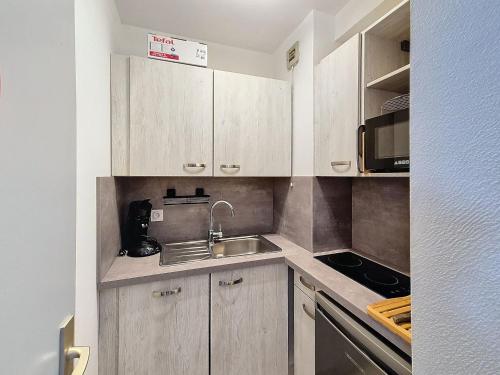 Elle comprend une petite cuisine avec des placards en bois et un évier. dans l'établissement Studio lumineux 5 pers, 50m des pistes avec balcons ensoleillés - FR-1-416-225, à La Toussuire