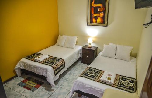 a room with two beds and a table with a lamp at Back Packer in Ibarra
