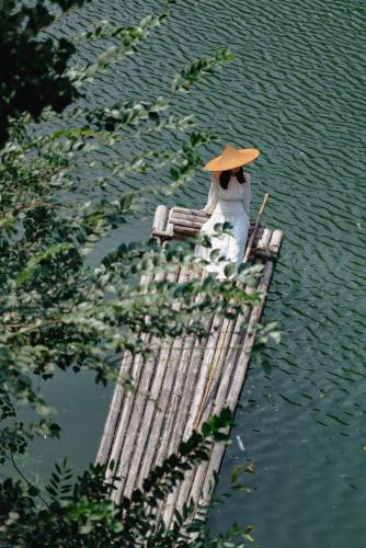 a person sitting on a bamboo raft in the water at Yakamoz Qianchuan Hotel in Lin'an