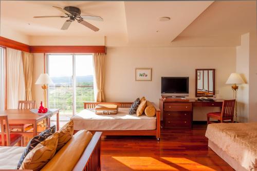 a living room with a bed and a desk and a tv at Kanucha Bay Hotel & Villas in Nago