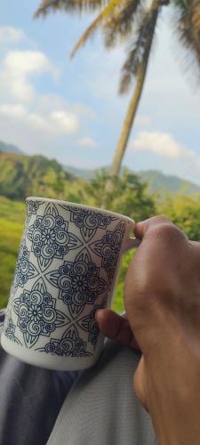 a person holding a coffee cup with a palm tree at Green valley home stay in Thekkady