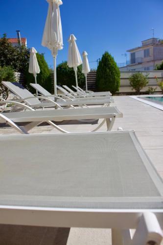 a row of white lounge chairs and umbrellas on a patio at Notos Luxury Studios in Katelios