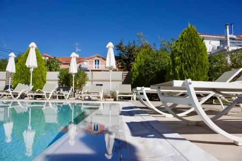 a swimming pool with white chairs and umbrellas at Notos Luxury Studios in Katelios