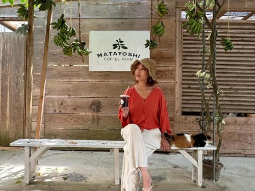 a woman sitting on a bench with a cat at Yambaru Experience Hotel Nunganiku in Higashi