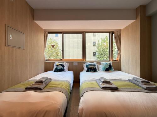 two beds in a room with a window at nestay inn tokyo tsukiji in Tokyo