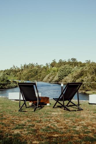 two chairs sitting on the grass next to a river at Quinta das Areias - Solar da Pena in Braga