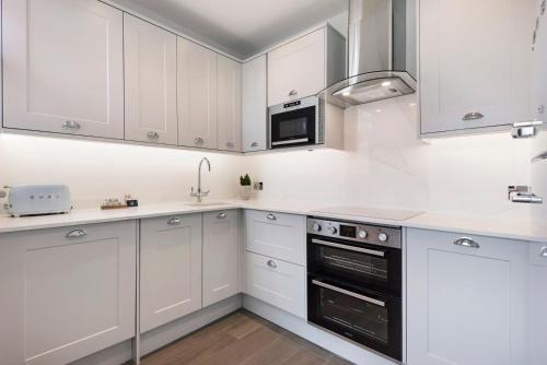 Una cocina blanca con gabinetes blancos y un microondas. en Modern and Bright Highgate Gem, en Londres