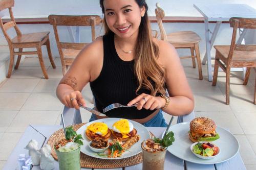a woman sitting at a table with a plate of food at Tipsy Sea View Apartment in Tanah Lot