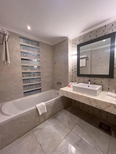 a bathroom with a tub and a sink and a mirror at Sataya Resort Marsa Alam in Marsa Alam City