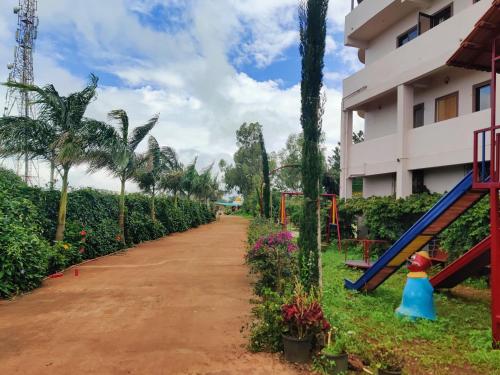 a dirt road next to a building with palm trees and a playground at Quinte Hills Residency in Panchgani