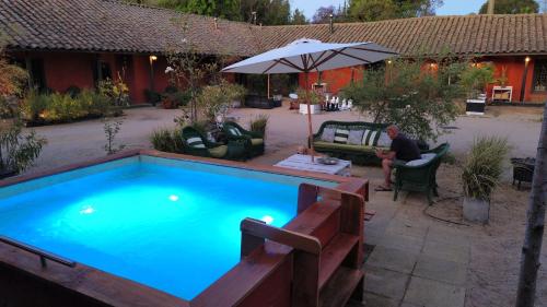 a man sitting under an umbrella next to a swimming pool at Casona Lo Aguirre , Hospedaje de Temporada Cálidas in Talagante