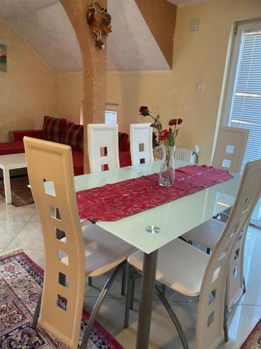 een witte eettafel met witte stoelen en een vaas met bloemen bij Apartman MILI in Požarevac