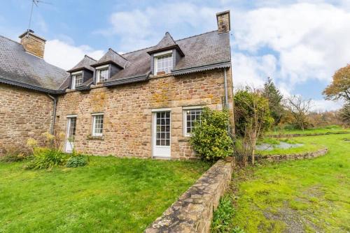 ein altes Backsteinhaus mit einem grünen Hof in der Unterkunft Charmante maison la Tissanderie a Saint-Carreuc in Saint-Carreuc