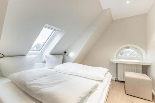 a white bedroom with a bed and an attic window at Ferienhaus Lee in Munkmarsch