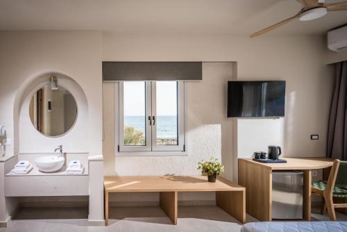 a room with a bathroom with a sink and a table at South Coast Hotel in Makry Gialos