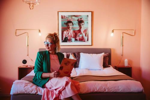 a woman sitting on a bed reading a book at Köpmans Boutique Hotel & Bistro in Höganäs