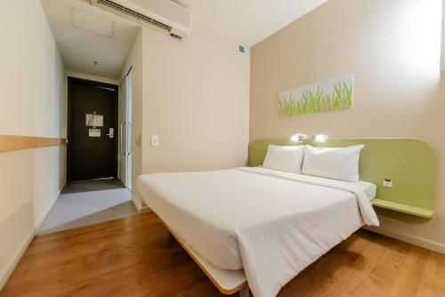 a bedroom with a large white bed with a green headboard at ibis budget Vitoria in Vitória