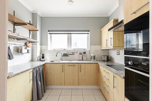 a kitchen with wooden cabinets and a large window at Bright and Stylish Riverside Haven in Canary Wharf in London