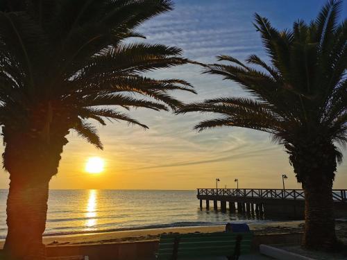 a pier on the beach with palm trees and the sunset at Villa Olympia in Paralia Katerinis