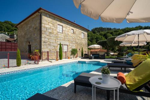 a swimming pool with chairs and an umbrella next to a building at Casa Zé Manel - Turismo Rural in Paranhos