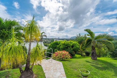 a garden with two palm trees and a pathway at Villa Blue Rock, piscine & vue imprenable in Rivière-Salée