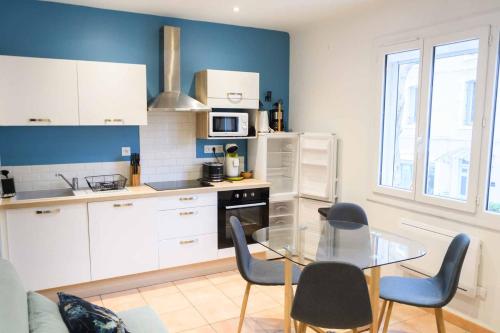 une cuisine avec des armoires blanches et une table en verre dans l'établissement Les volets blancs, à Lamalou-les-Bains