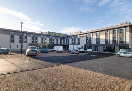 a large building with cars parked in a parking lot at B&B HOTEL Massieux Genay in Genay