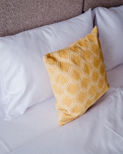a yellow pillow on a bed with white pillows at Arche Nałęczów & SPA dawne Sanatorium Milicyjne in Nałęczów